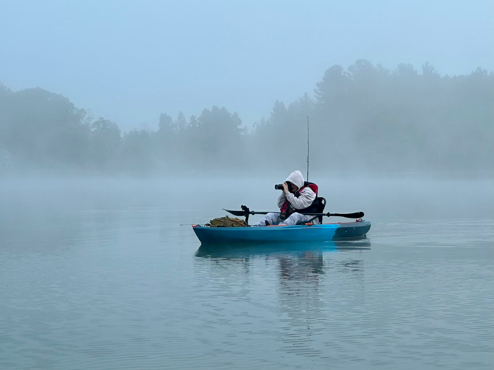 Two people fishing from a canoe in the dawn mist